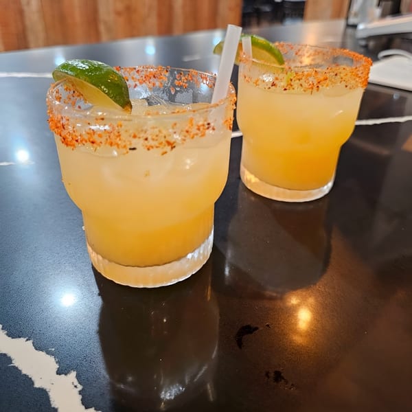 Two Wael's Mediterranean Cuisine margaritas with chili-lime rims and lime wedges on a dark table.