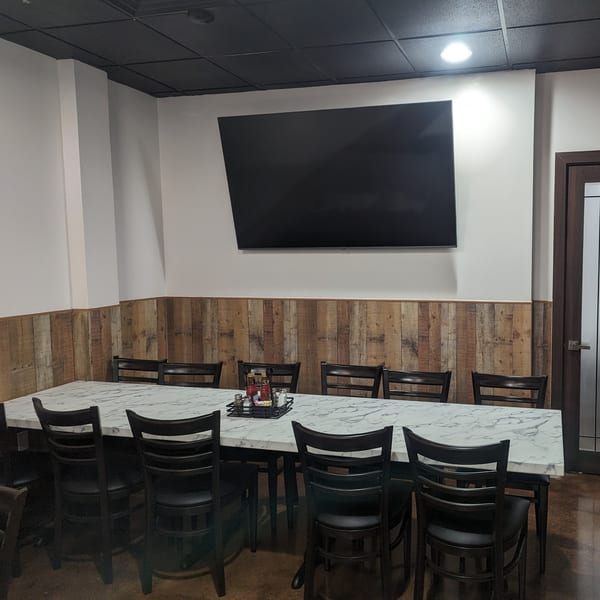 Long marble-top table with black chairs, wood paneling, and a large TV in Wael's Mediterranean Cuisine.