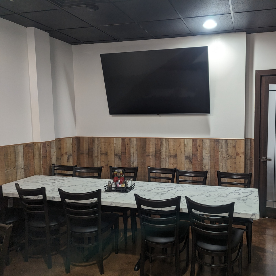 Long marble-top table with black chairs, wood paneling, and a large TV in Wael's Mediterranean Cuisine.