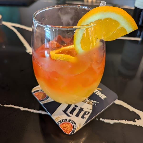 A vibrant orange and yellow layered drink with an orange slice and straw on a coaster.