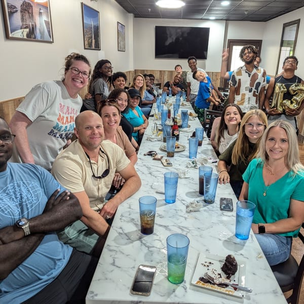 Diverse group of people smiling at a long table with drinks and dessert at Wael's Mediterranean Cuisine.
