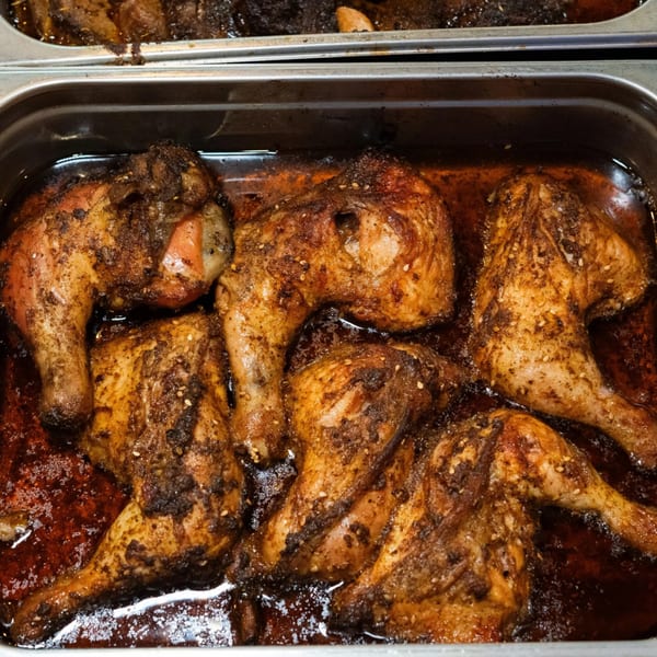 Several pieces of Mediterranean-spiced chicken, glistening with sauce, in a metal serving tray.
