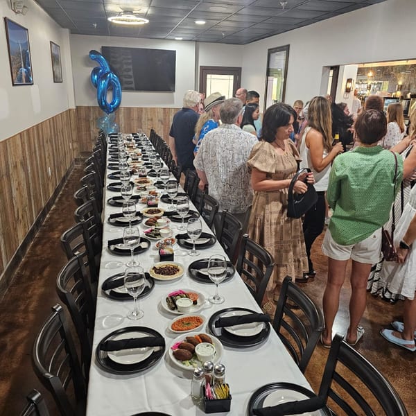 Guests mingle around a long table set with Mediterranean dishes and place settings at Wael's Cuisine.
