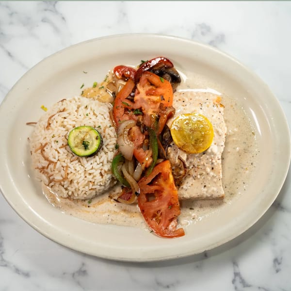 Mediterranean dish with rice, zucchini, fish in cream sauce, and roasted vegetables on a white plate.
