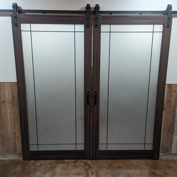 Dark wood barn doors with frosted glass panels and black hardware, set against a white wall.