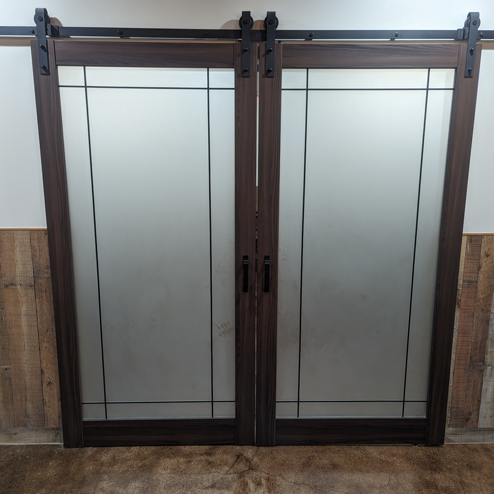 Dark wood barn doors with frosted glass panels and black hardware, set against a white wall.
