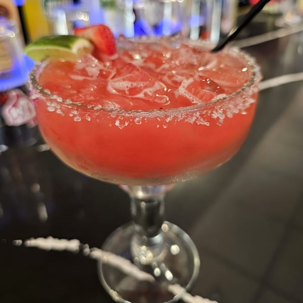 A vibrant red strawberry margarita with a salted rim, lime, and strawberry garnish.