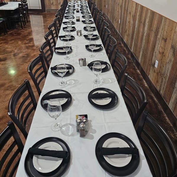 Long dining table set with white tablecloths, black plates, and wine glasses at Wael's Mediterranean Cuisine.